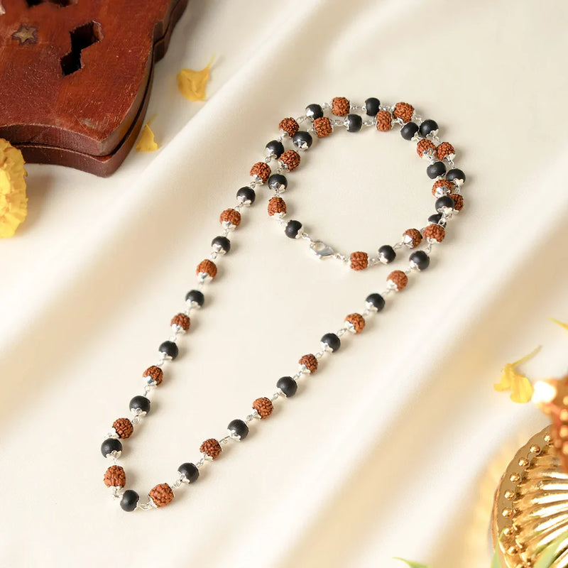 Rudraksha and Karungali mala with silver capping laid flat on cream fabric with a wooden stand and flowers