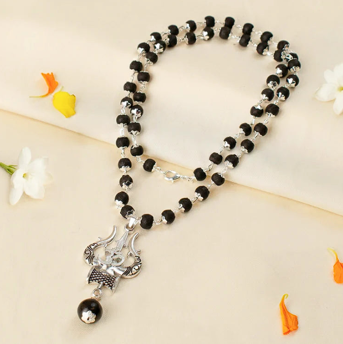 Karungali mala with silver Om Shiva Trishul pendant laid flat on cream fabric with flowers
